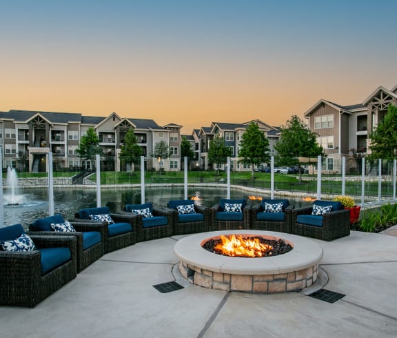 a firepit and seating area in front of an apartment complex with a fountain