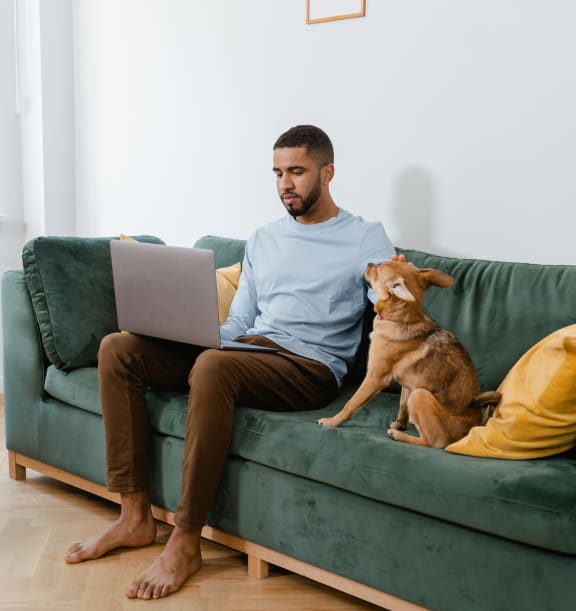a man sitting on a couch with a dog and using a laptop