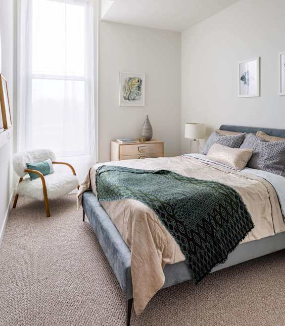 A bedroom with a bed, chair, and nightstand at The Pennsylvanian Apartments, Pittsburgh, Pennsylvania