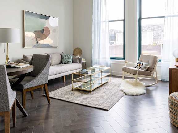 A modern living room with a grey sofa, a wooden dining table and chairs, a rug, and a painting on the wall. at The Pennsylvanian Apartments, Pittsburgh, Pennsylvania