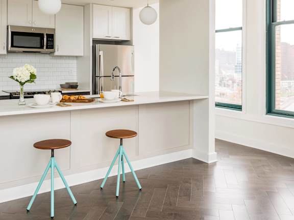 A kitchen with a white counter and two blue stools. at The Pennsylvanian Apartments, Pittsburgh, Pennsylvania