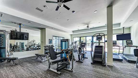 a gym with treadmills and other exercise equipment in a building with windows at Imperial Crossing Luxury Apartment Homes, Bonita Springs, FL