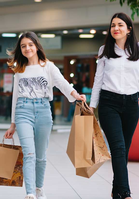 Two women walking in a mall carrying shopping bags.