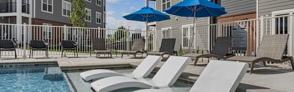 A pool with sun loungers and umbrellas in front of a building.