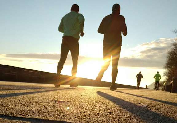 Two people jogging on a road with the sun setting in the background.