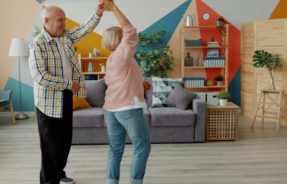An elderly couple dancing together in a living room.