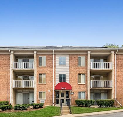 A red brick apartment building with a red awning and a green lawn in front.