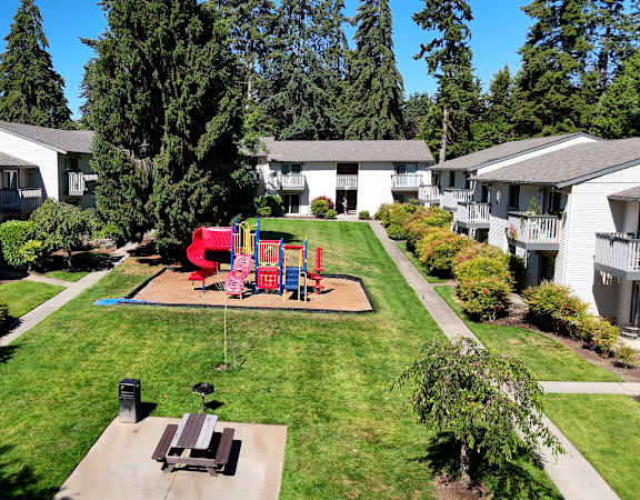 A playground with a slide and swings in the middle of a grassy area.