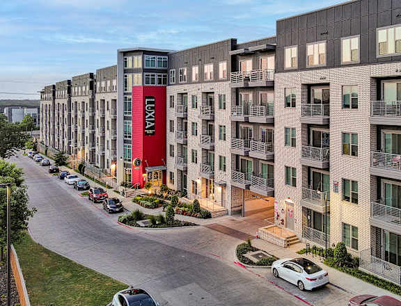 A street view of a residential area with apartment buildings and cars parked on the side of the road.