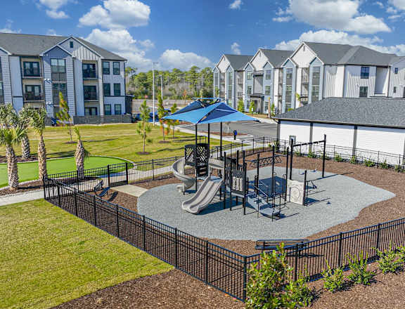 A playground with a slide and a swing set in front of a building at Evolve St. James Apartment Homes Apartments, Southport, NC, 28461