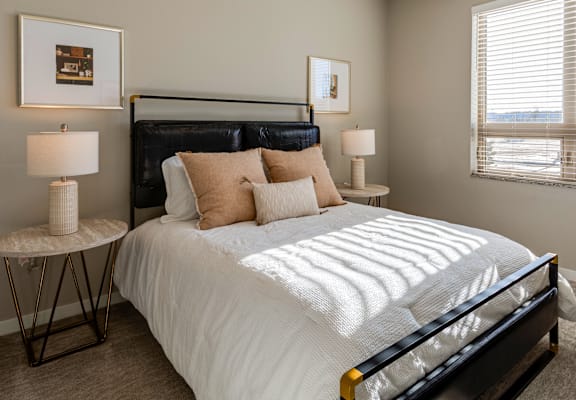 A bedroom with a large bed, two lamps, and a picture frame on the wall.