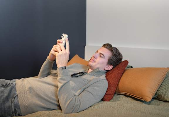 A man is lying on a bed and taking a selfie with his phone.