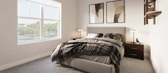 A bedroom with a large bed and a window overlooking a street.at The Landing at Hub City, Plymouth, 53073