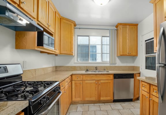 Apartment kitchen with stainless steel appliances, tan counter tops, and wood cabinets.