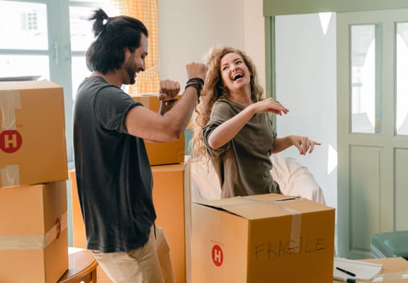Happy couple dancing and laughing while packing moving boxes in a living room.