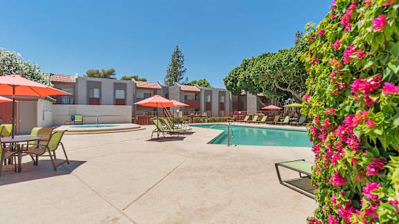 A pool area with chairs and umbrellas surrounded by a wall of flowers.