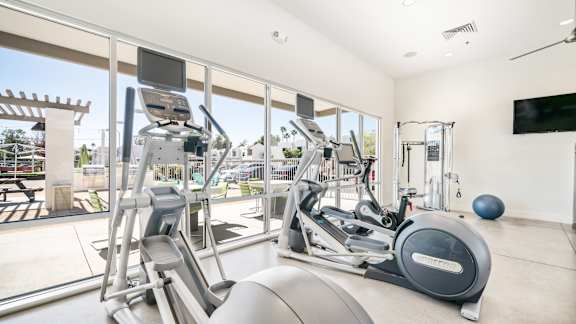 a gym with cardio machines and a large window with a view of the pool