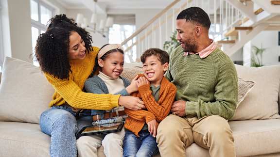 A family of four is sitting on a couch together.