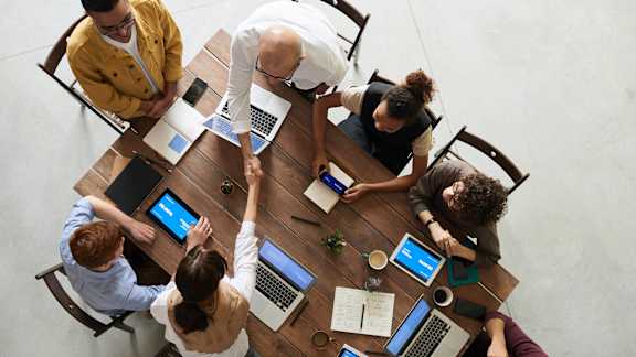 Aerial view of a table of people with their laptops and note pads having a meeting