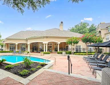 a swimming pool in front of a house with a patio with chairs