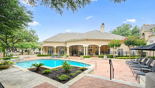 a swimming pool in front of a house with a patio with chairs