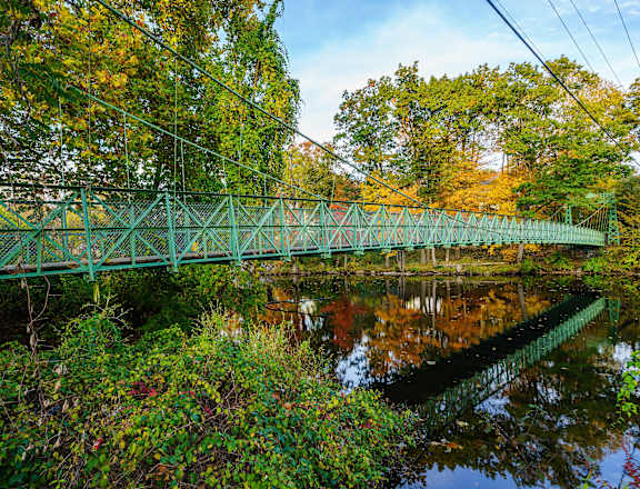 A green bridge over a calm body of water surrounded by trees.