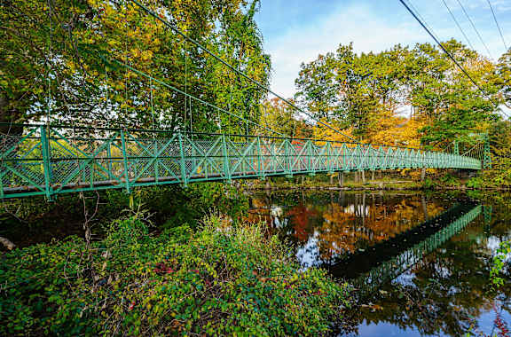 A green bridge over a calm body of water surrounded by trees.