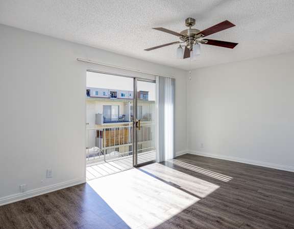 an empty living room with a ceiling fan and sliding glass doors to a balcony