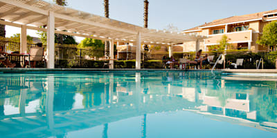 A swimming pool with a white canopy and people sitting on the poolside.