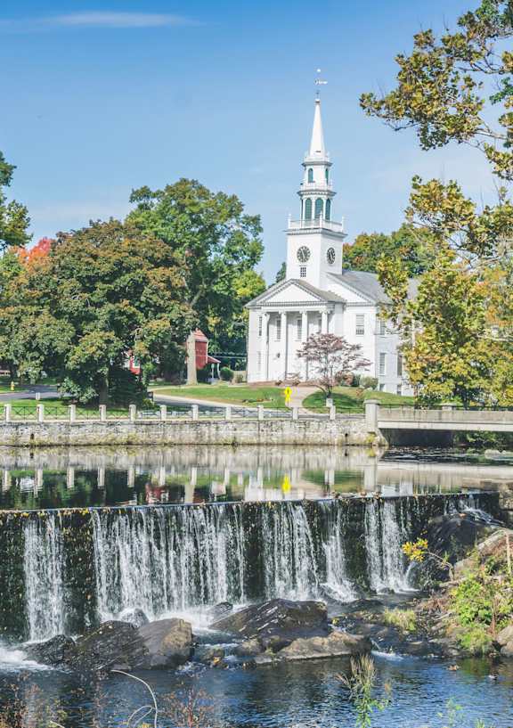 A church with a steeple stands behind a waterfall.