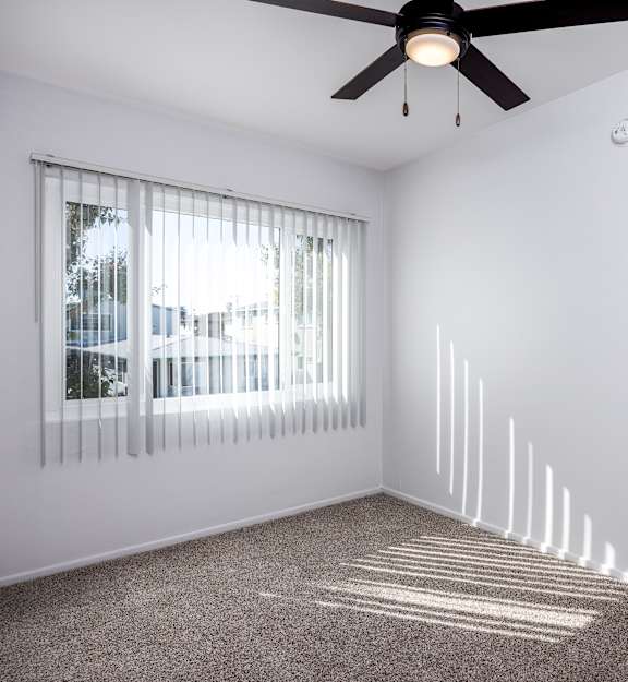 A room with a ceiling fan and a window with blinds.