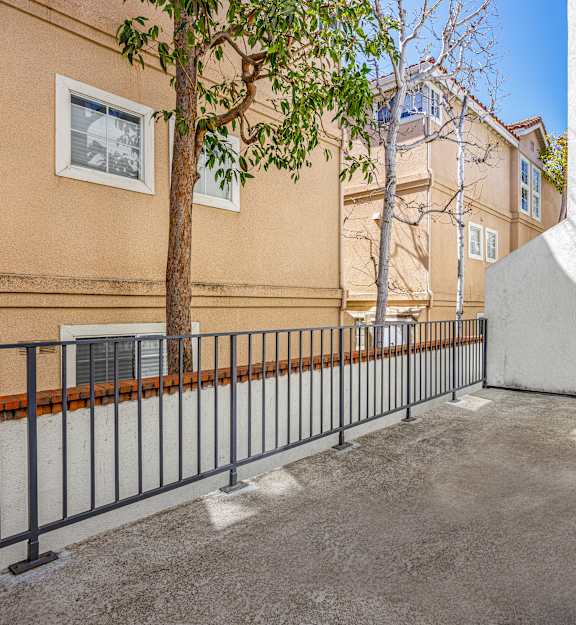 A tree is in front of a building with a white wall and a black fence.