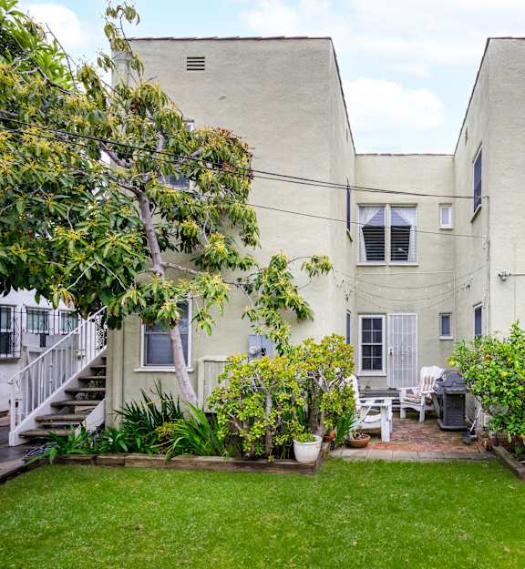 the backyard of a white apartment building with a lawn and plants