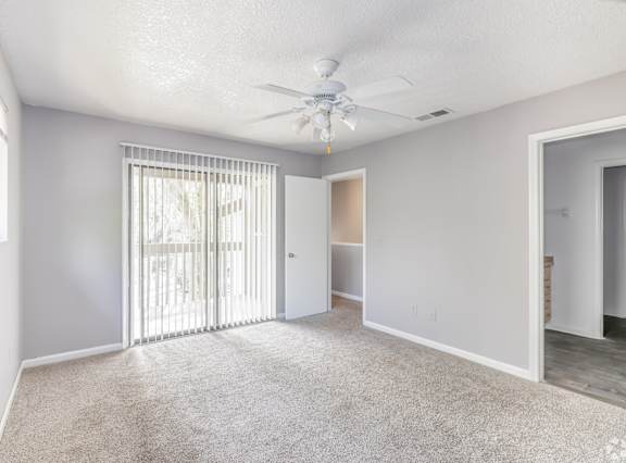 A room with a ceiling fan and sliding glass doors.