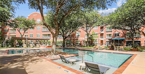 A pool surrounded by trees and chairs in front of a red building.