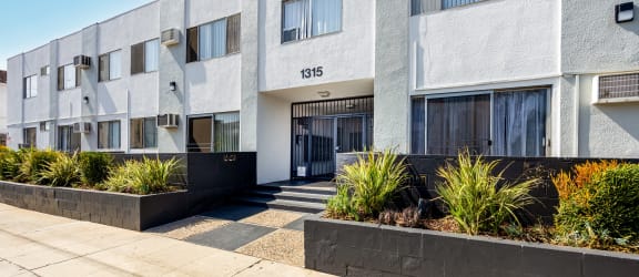 an apartment building with a sidewalk and plants in front of it