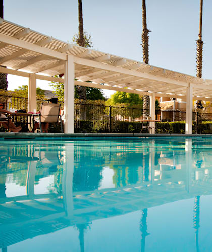 A swimming pool with a white canopy and people sitting on the poolside.
