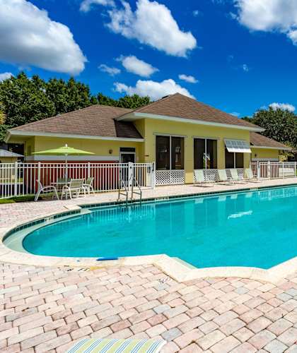 A swimming pool surrounded by a brick patio and a yellow building in the background.