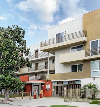 an apartment building with a sidewalk and a tree in front of it