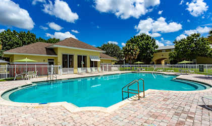 A swimming pool surrounded by a brick patio and a yellow building in the background.