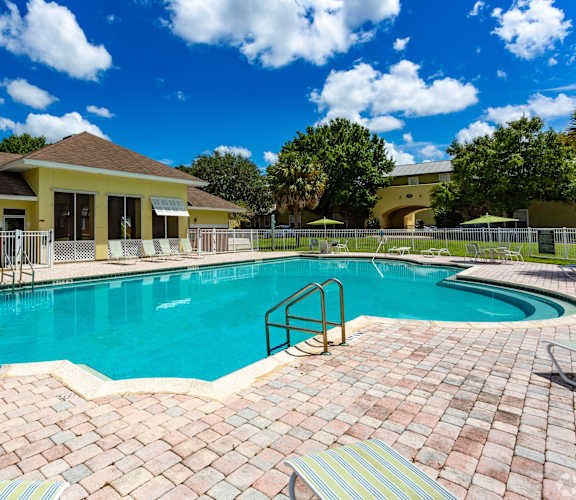 A swimming pool surrounded by a brick patio and a yellow building in the background.