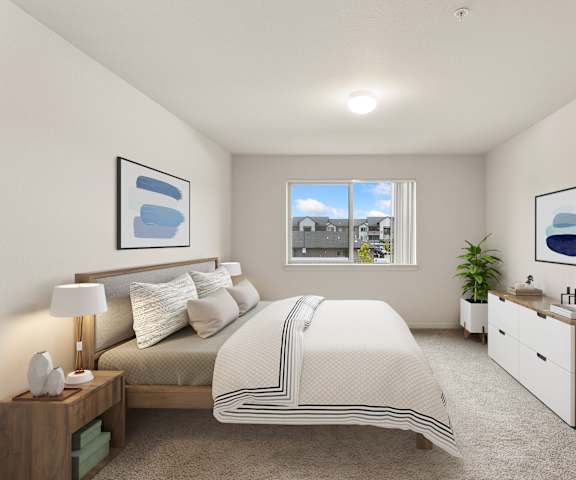A bedroom with a large bed, nightstand, and a window overlooking a cityscape.