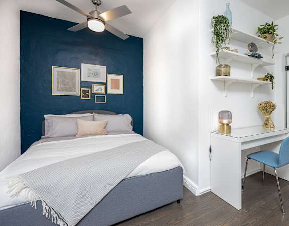 a bedroom with a bed and desk in front of a blue wall