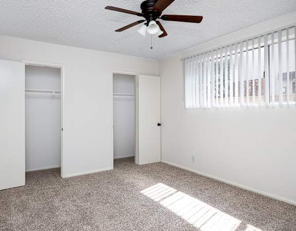 an empty living room with a ceiling fan and two closets
