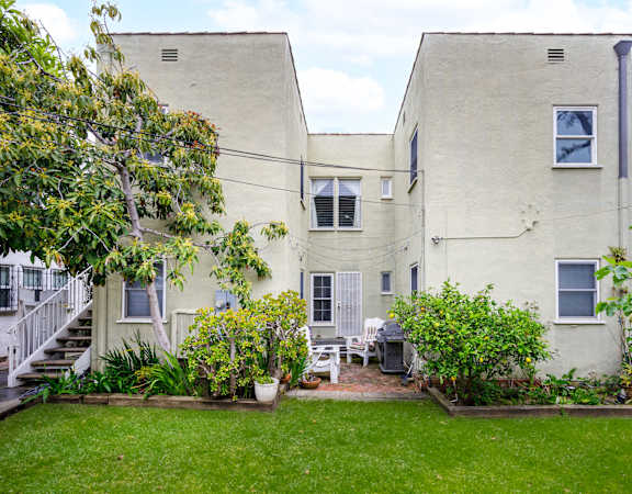 the backyard of a white apartment building with a lawn and plants