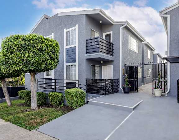 a grey building with a driveway and a tree in front of it