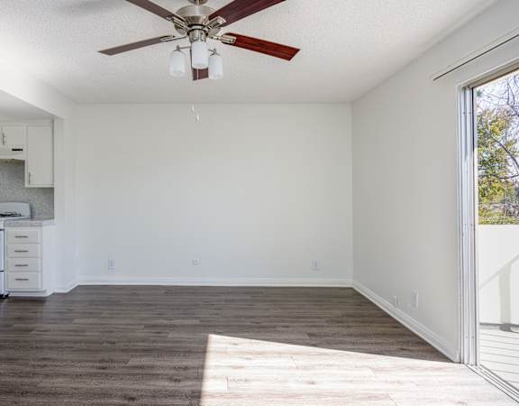 an empty living room with a ceiling fan and a kitchen