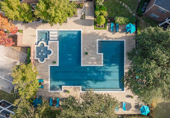An aerial view of a swimming pool surrounded by trees and a small building.
