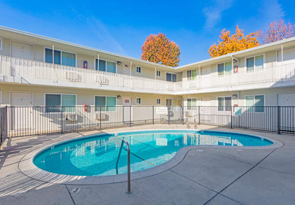 A swimming pool is surrounded by a black fence in front of a white building.