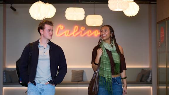 A man and a woman are standing in front of a Calico sign.